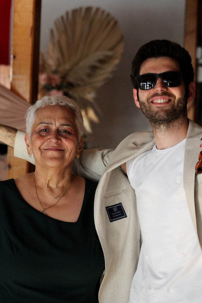 A cheerful mother and son pair posing together indoors in Berlin, showcasing stylish attire and sunglasses.