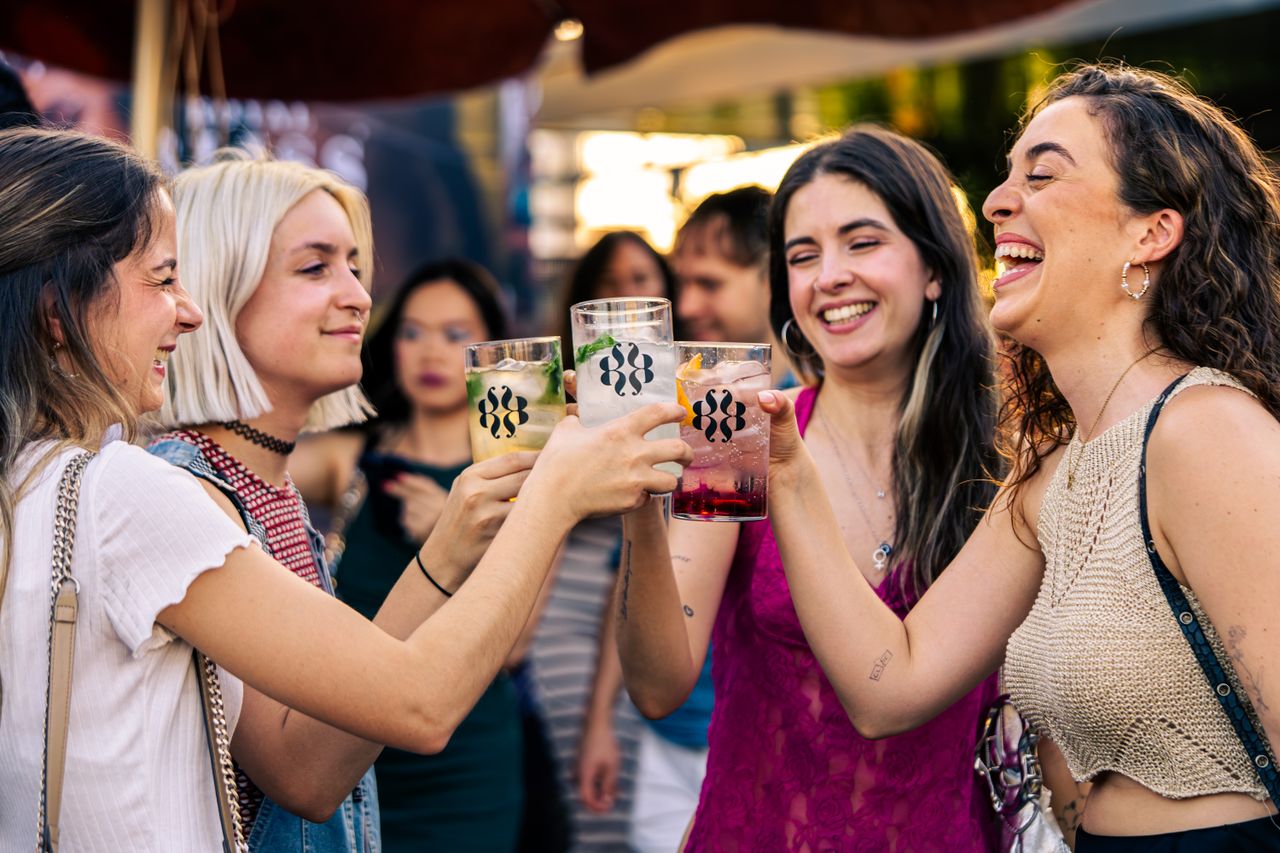 Crafting Captivating Headlines: Your awesome post title goes here Young women laughing and clinking glasses in a lively outdoor setting, enjoying a festive atmosphere.