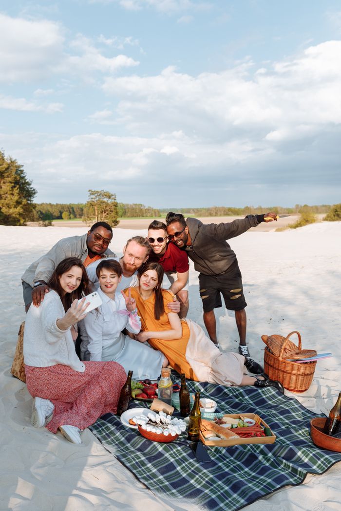 Group of friends having a joyful picnic on the beach, capturing moments with a selfie.